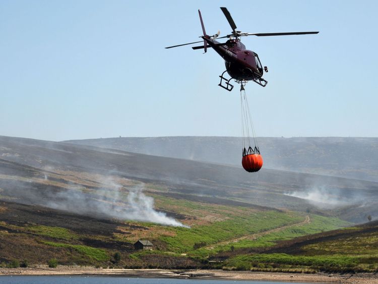 A helicopter carries a container with water from Upper Swineshaw Reservoir before dumping the water onto smouldering fires on Saddleworth moor 