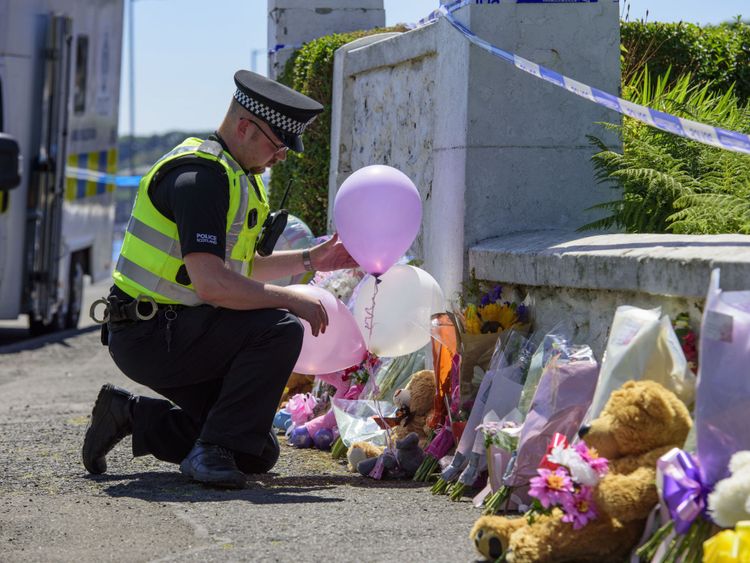 A police officer leaves balloons near a house on Ardbeg Road 