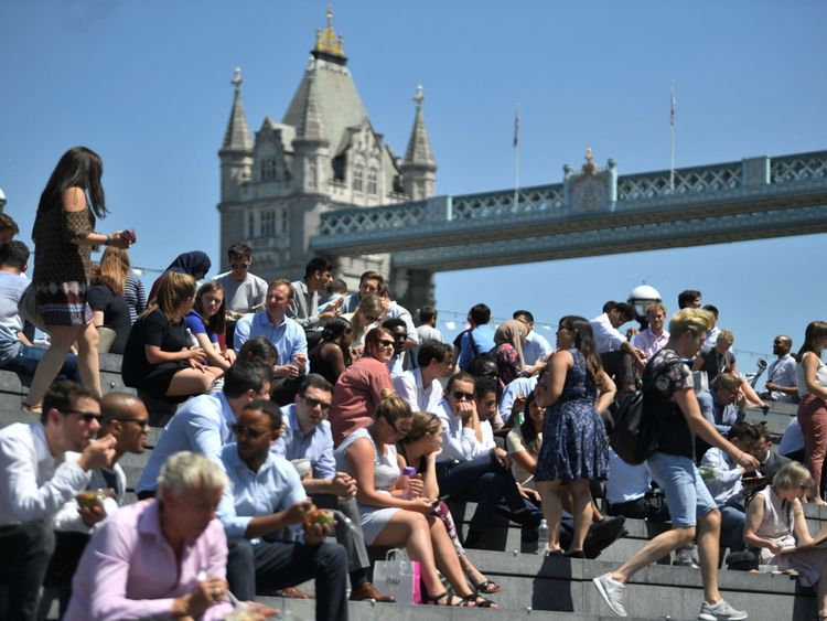 People enjoy their lunch break in the sunshine near Tower Bridge in London