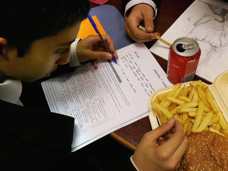 LONDON - OCTOBER 5: In this photo illustration a school student eats a hamburger and chips as part of his lunch which was brought from a fast food shop near his school, on October 5, 2005 in London, England